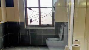 Casa de banho com cabine de duche em vidro, sanita e janela.