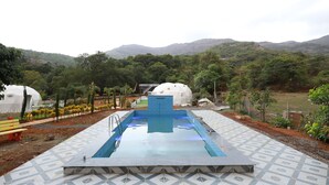 A swimming pool with a geometric tile pattern, surrounded by a landscaped area with trees and a view of hills. - Harmony Hills (Paud)