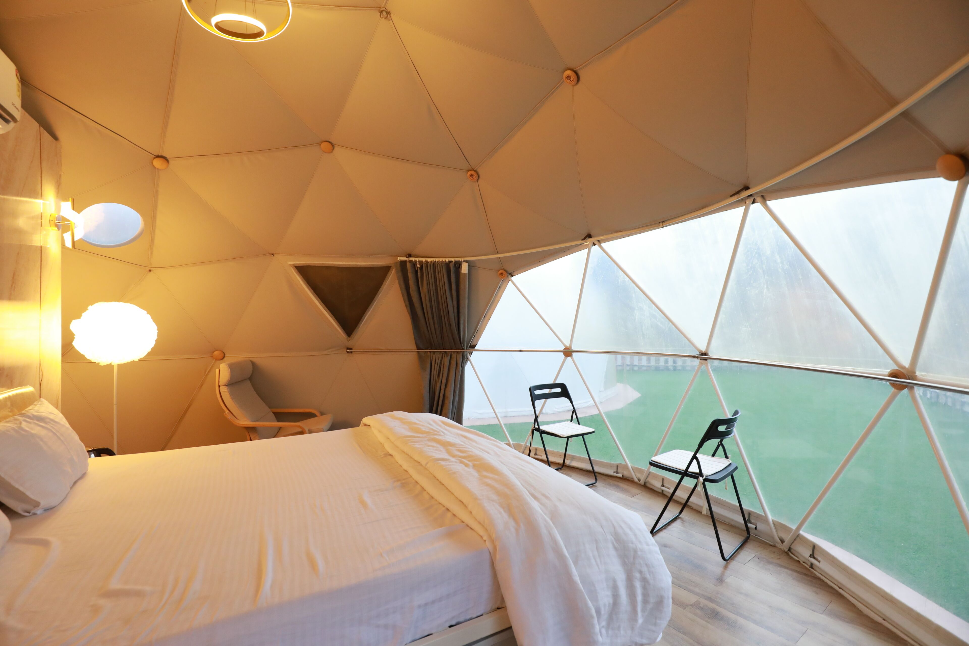 A tent-style room with a bed, chairs, and a view of a green field.