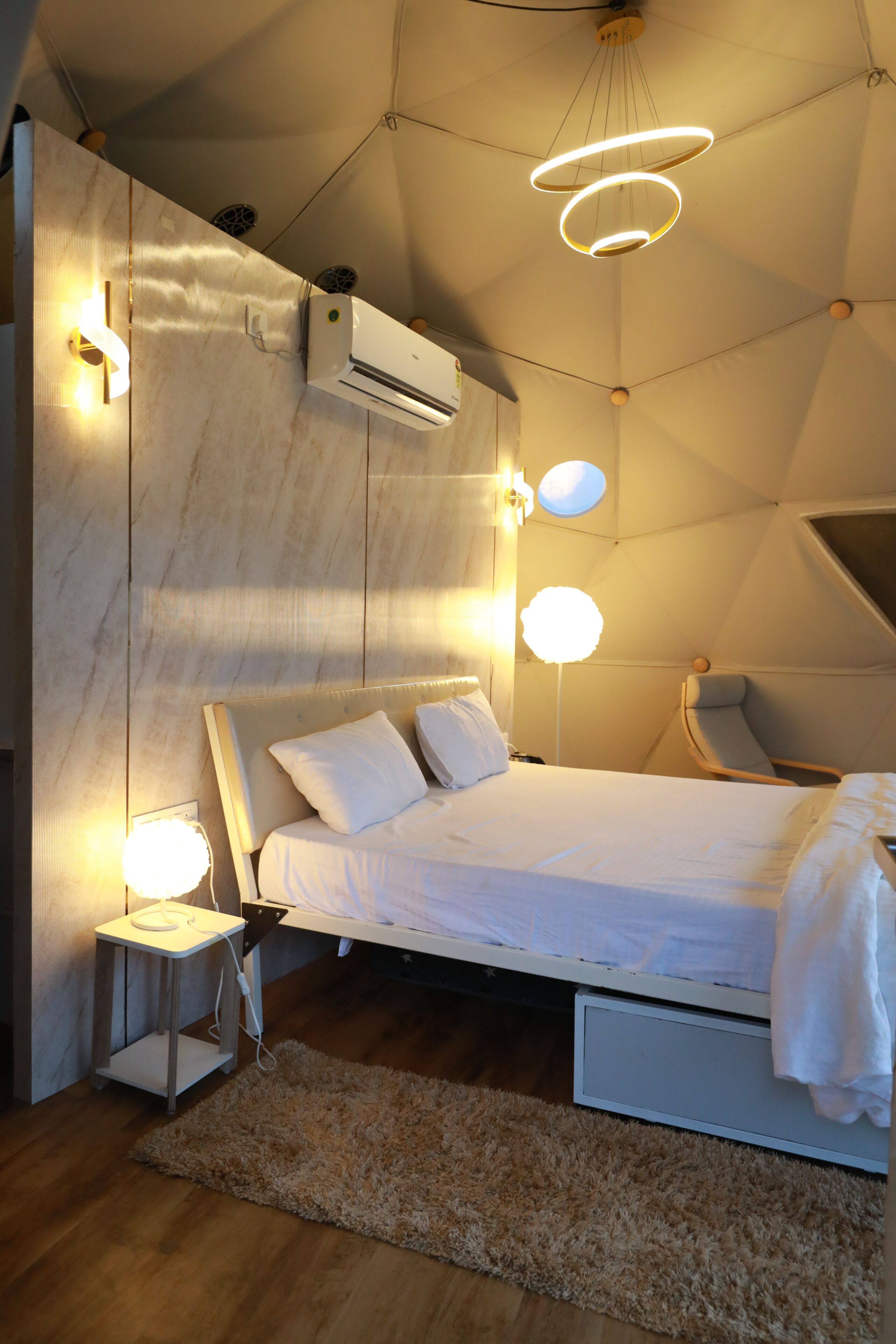 A modern bedroom with a bed, bedside tables, a wall-mounted air conditioner, and a ceiling light fixture.