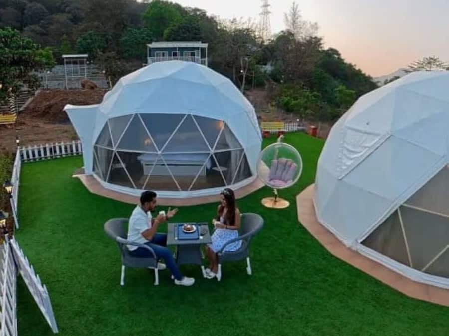 Two geodesic dome structures with a grassy lawn, a dining table, and chairs.