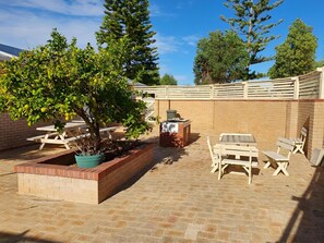 An outdoor patio area with a brick floor, wooden picnic tables, and a barbecue grill. - Ocean Beach Chalet 18 (Jurien Bay)
