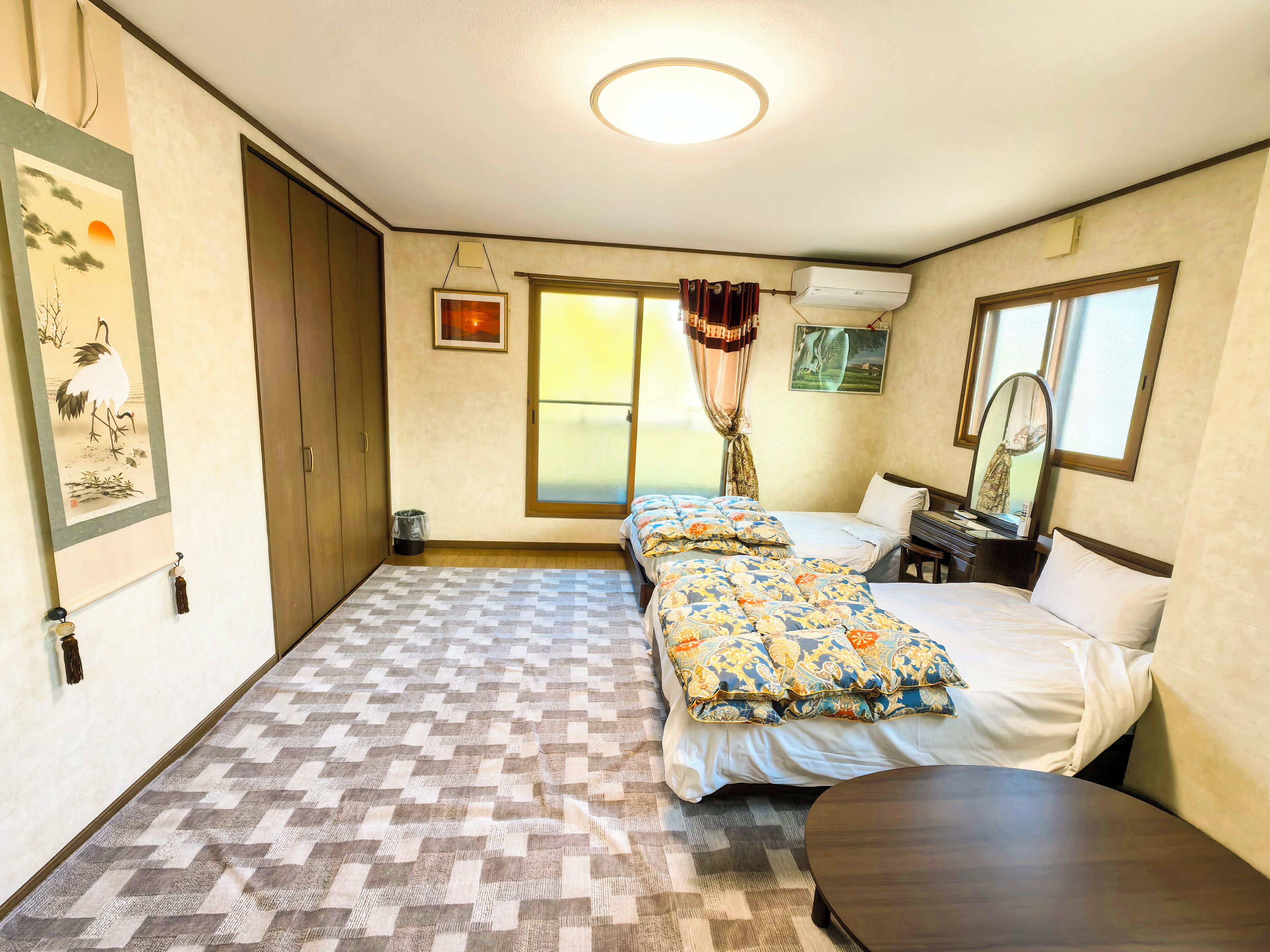 Una habitación de hotel con piso a cuadros, dos camas con ropa de cama estampada, una mesita, un espejo y obras de arte en las paredes.