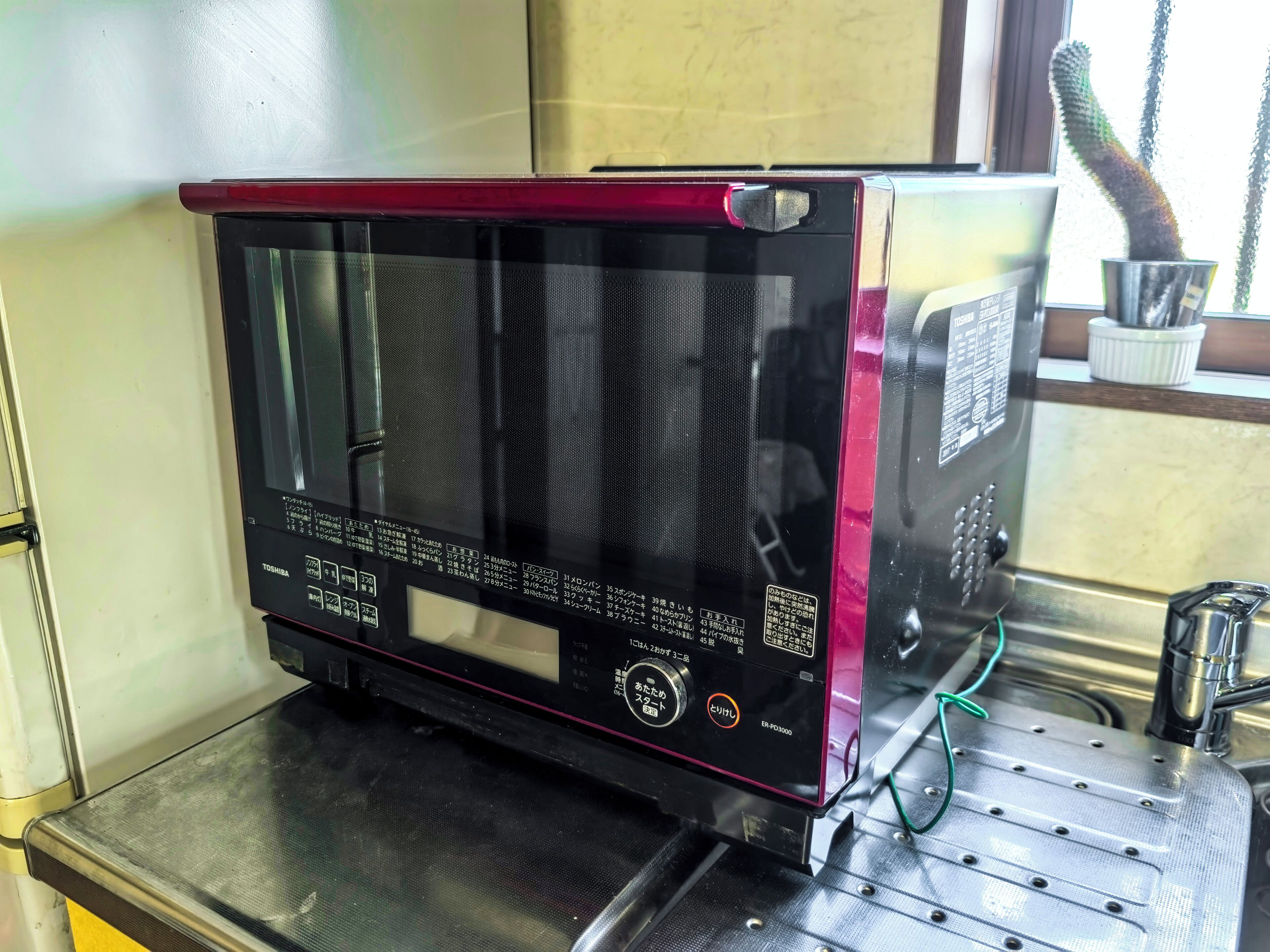 Een Toshiba magnetron met een digitaal display, geplaatst op een metalen oppervlak.
