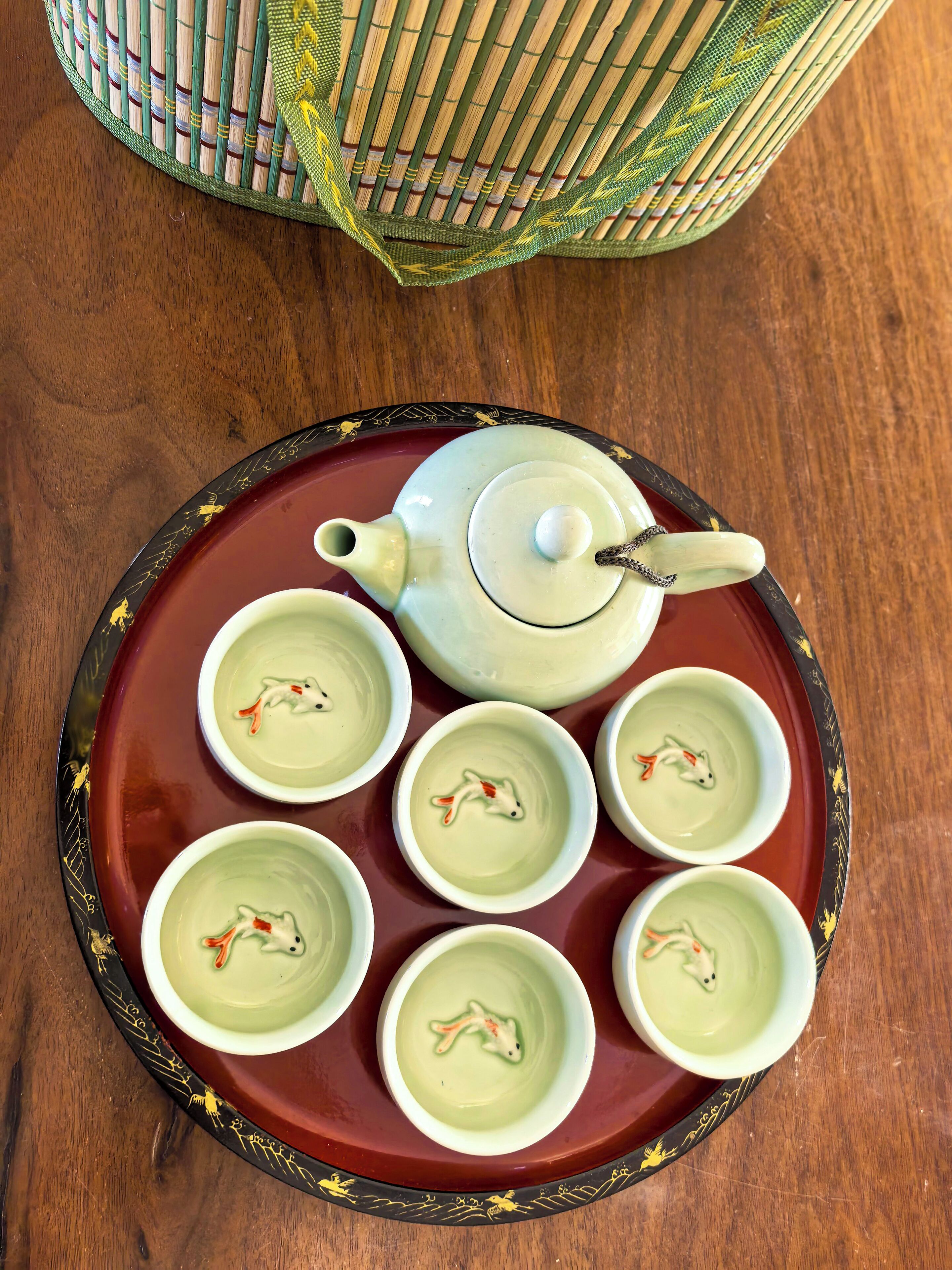 Een theepot en zes kopjes op een dienblad met een decoratieve rand.