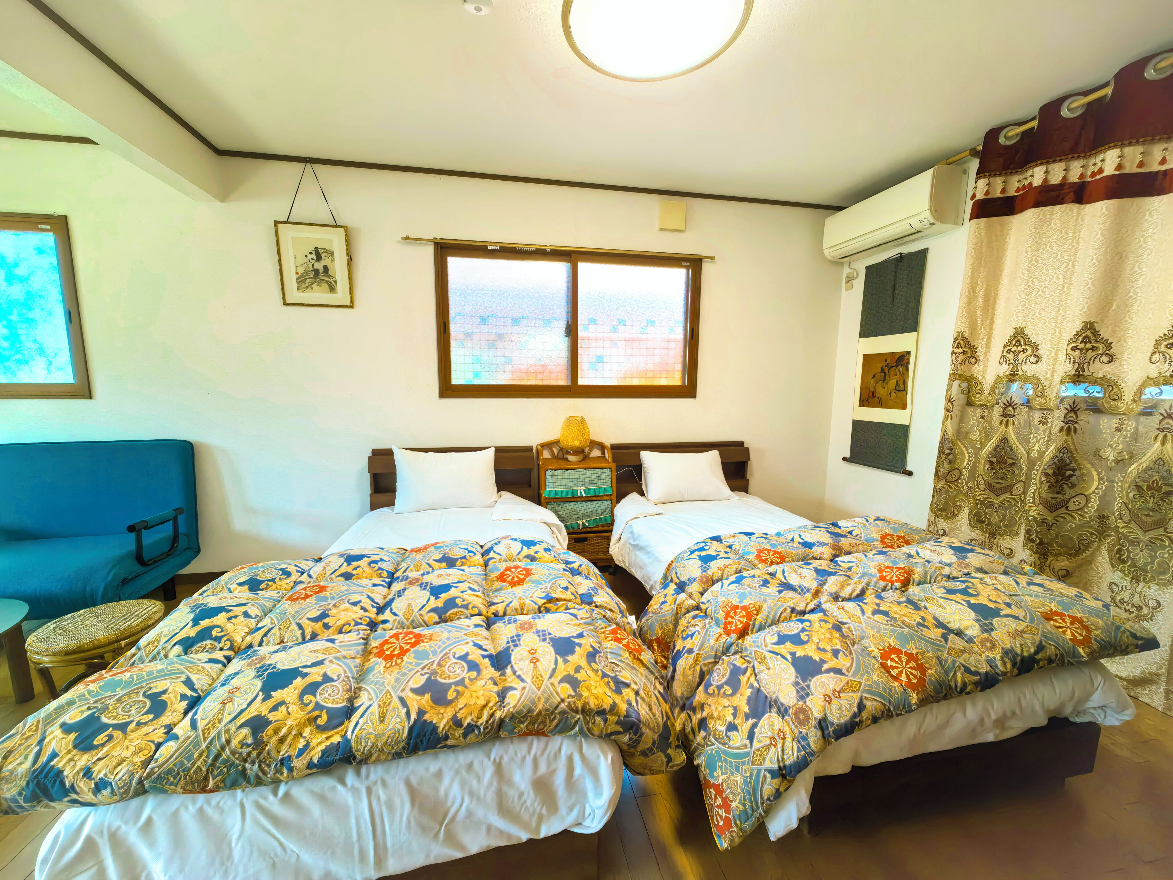 Hotelkamer met twee bedden, een raam, een airconditioner en een blauwe bank.