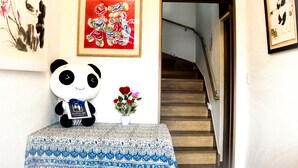 A room with a panda plush toy, a framed painting, and a staircase. - Onsengunyado (Toon)