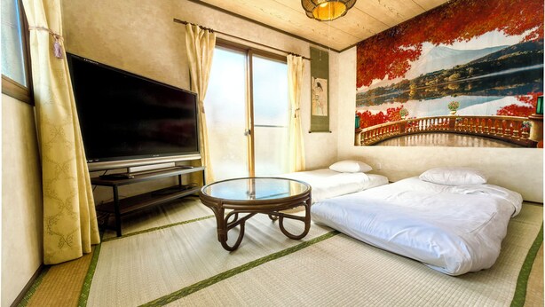 A hotel room with a bed, a television, a table, and a painting of a landscape. - Onsengunyado (Toon)