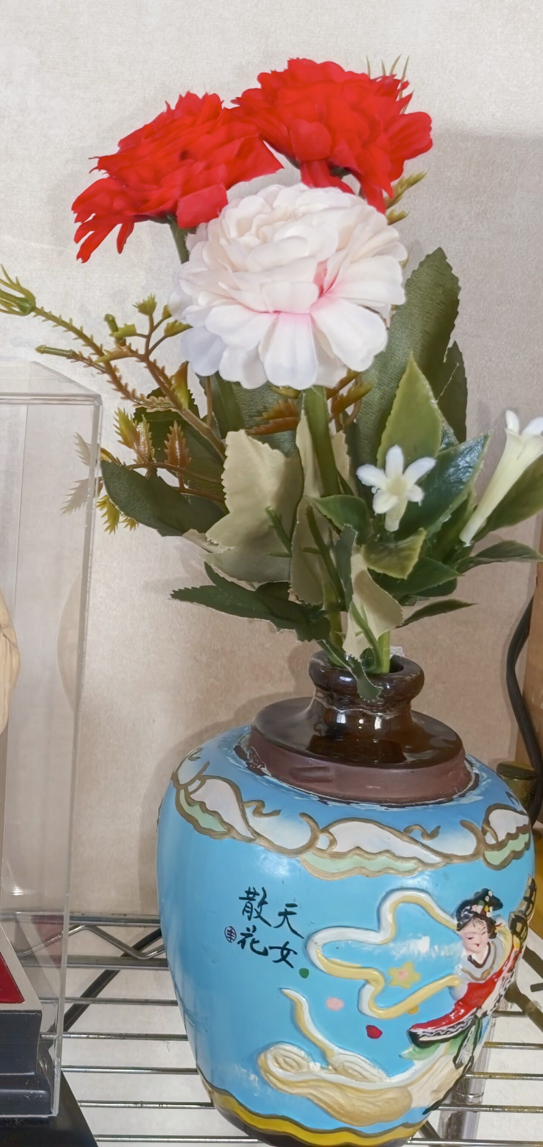 A vase with a decorative design and a figure, containing red and white flowers.