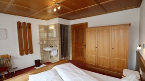 A bedroom with a large bed, wooden wardrobe, a bathroom with a sink and mirror, and a wooden chair. - Cozy Apartment With a Beautiful View (Kappl)