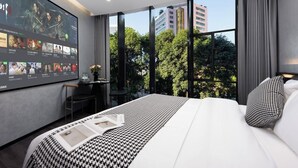 Una habitación de hotel moderna con una cama grande, un escritorio y un televisor en la pared mostrando diferentes programas.