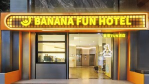 Exterior del hotel Banana Fun, con un letrero de neón, puertas de vidrio y un interior moderno visible a través de la entrada.