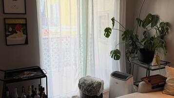 A living room with a sofa, a coffee table, a plant, a radiator, and a wall-mounted shelf with bottles.