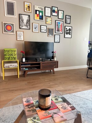 A living room with a TV, framed artwork on the wall, a coffee table with books, and a small table with a vase and flowers. - Perfect 2-bedroom apartment in charming residential area in mid city Los Angeles (Los Angeles)