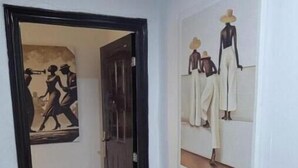 Een gang met een deur die leidt naar een kamer, een deurmat waarop 'home' staat en twee kunstwerken met afbeeldingen van mensen.