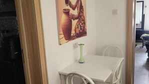 Een eetgedeelte met een witte tafel en stoelen, een schilderij aan de muur en een groene vaas.