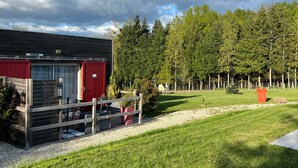 Ein rotes Gebäude mit eingezäunter Fläche, einer grünen Wiese und einem Wald im Hintergrund.