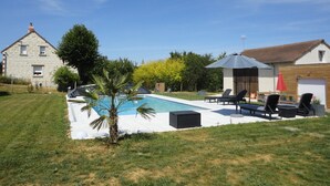 Ein Swimmingpool mit Liegestühlen, einer kleinen Palme und einem Steinhaus im Hintergrund.