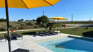 A swimming pool with lounge chairs and an umbrella, surrounded by a landscaped garden. - Le Hameau du Peu - Happy Cottage with Shared Pool (Châteauvieux)