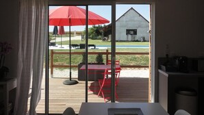 A room with a sliding glass door leading to an outdoor deck with a red umbrella, a table, and chairs. - Le Hameau du Peu - Happy Cottage with Shared Pool (Châteauvieux)