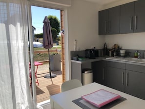 A compact kitchen with grey cabinets, a small dining table, and a sliding glass door leading to an outdoor area with a patio table and umbrella.