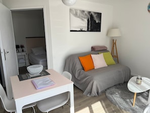 A bedroom with a bed, a desk, a chair, a small table, a lamp, and a painting on the wall.