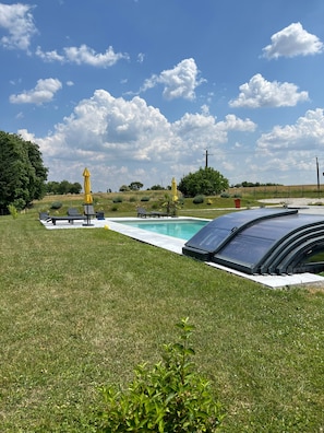 A swimming pool with a covered deck, surrounded by grass, with two yellow umbrellas and lounge chairs.
