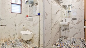 A bathroom with a toilet, shower, sink, and marble walls. - Hotel Elysian at Delhi Airport  (New Delhi)