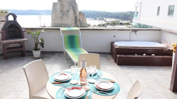 Un balcón con una mesa lista para comer, una parrilla, una hamaca y vistas a una torre histórica.