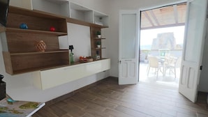 Una habitación con suelo de madera, pared blanca y una puerta corredera que da a un espacio exterior con vistas.