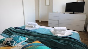 Un dormitorio con cama, cómoda, televisor y puerta.