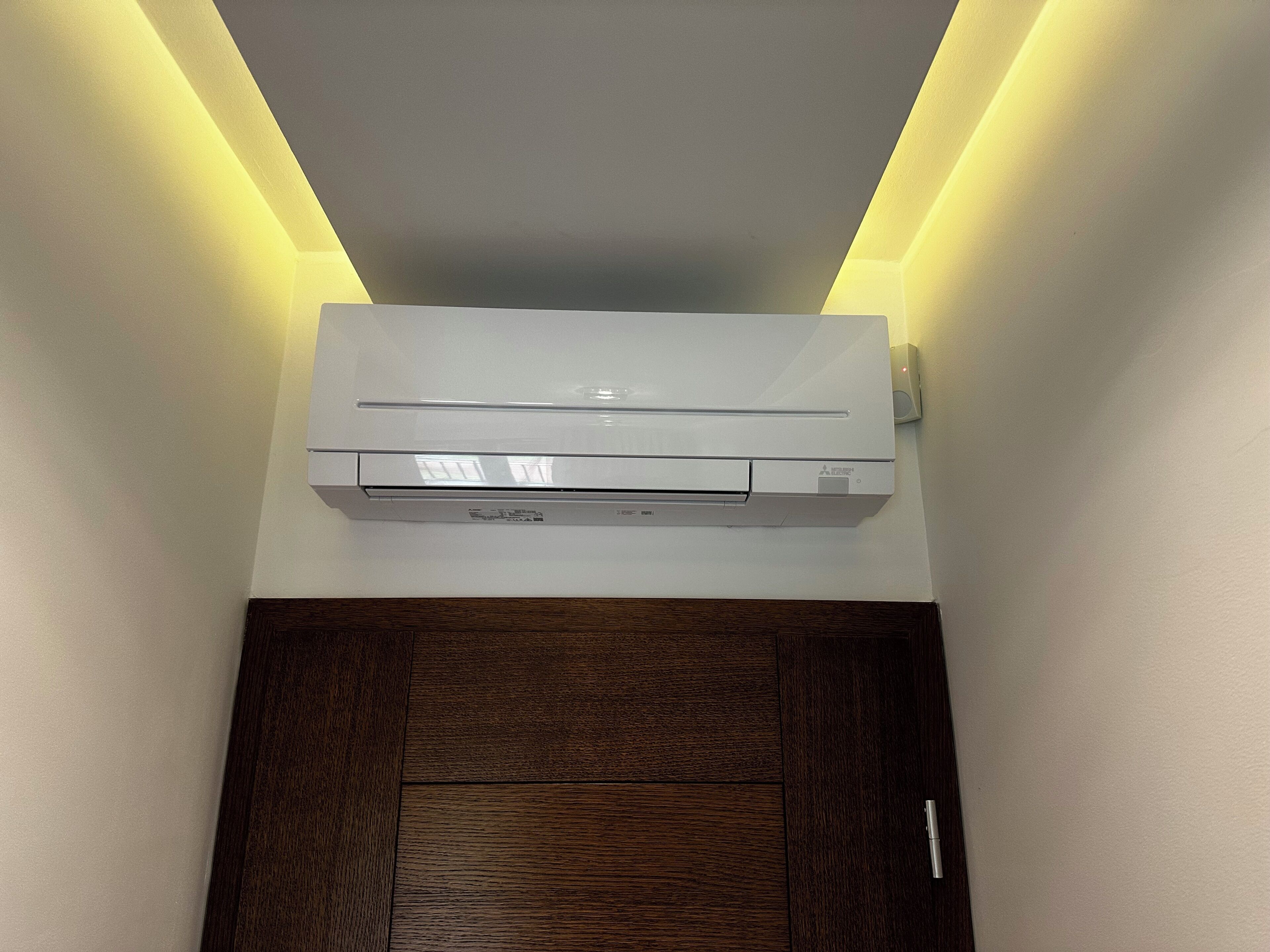Un condizionatore d'aria bianco fissato a una parete, con una porta in legno sottostante.