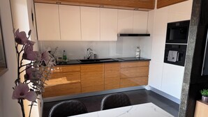 A modern kitchen with wooden cabinets, a black countertop, and a white marble dining table. - OLIMPIC Apartament Suwałki AirCon Garage Self-Check In/Out (Suwałki)