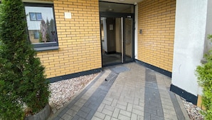 A building entrance with a brick facade, a glass door, and a small potted plant. - OLIMPIC Apartament Suwałki AirCon Garage Self-Check In/Out (Suwałki)