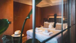 Quarto de hotel com cama, almofadas e um chapéu em uma cadeira.