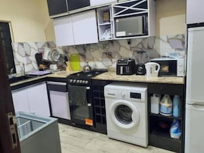 A compact kitchen with a gas stove, microwave, toaster, and a washing machine.