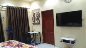 A bedroom with a bed, a desk, a chair, a TV, and a door. - Charming Executive Suite with Garden Views at AJALA Lodge, Badagry (Badagry)