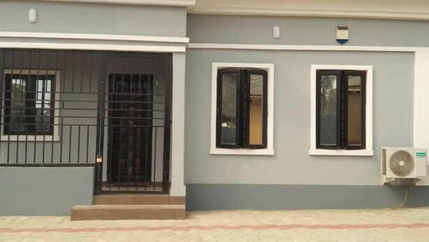 A building with a grey facade, a tiled roof, a gated entrance, and a small air conditioning unit mounted on the wall. - Charming Executive Suite with Garden Views at AJALA Lodge, Badagry (Badagry)