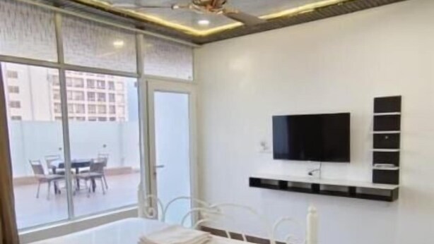 A modern bedroom with a bed, a ceiling fan, a TV mounted on the wall, and a view of the outside. - Joey's hostel Jaipur (Jaipur)