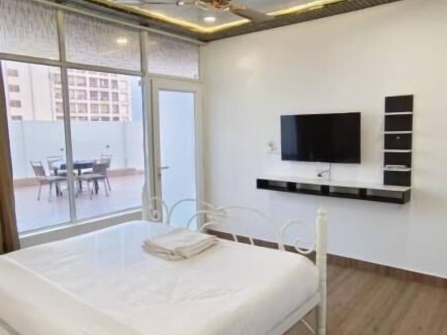Un dormitorio moderno con cama, ventilador de techo, televisor montado en la pared y vistas al exterior.