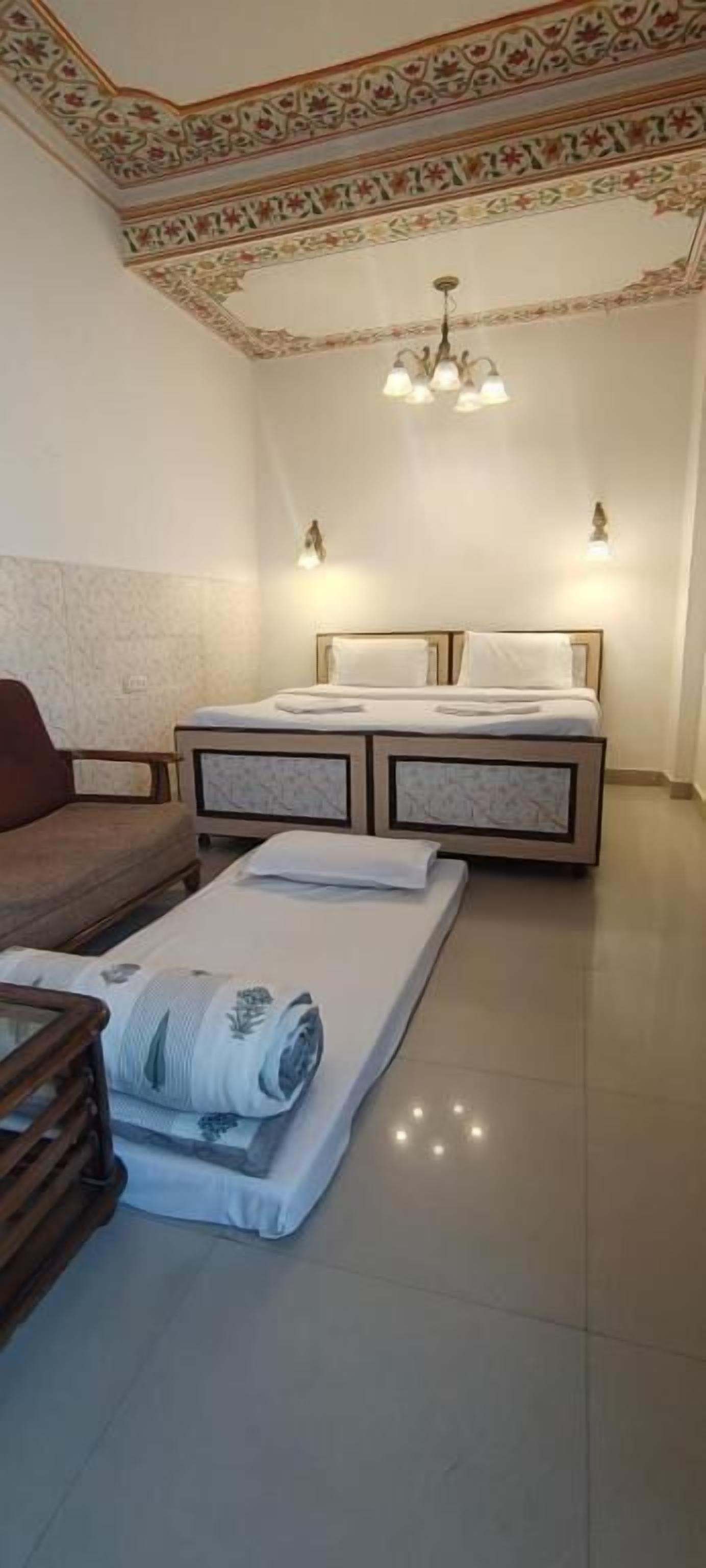 A bedroom with a double bed, a wooden side table, a sofa, and a patterned ceiling.