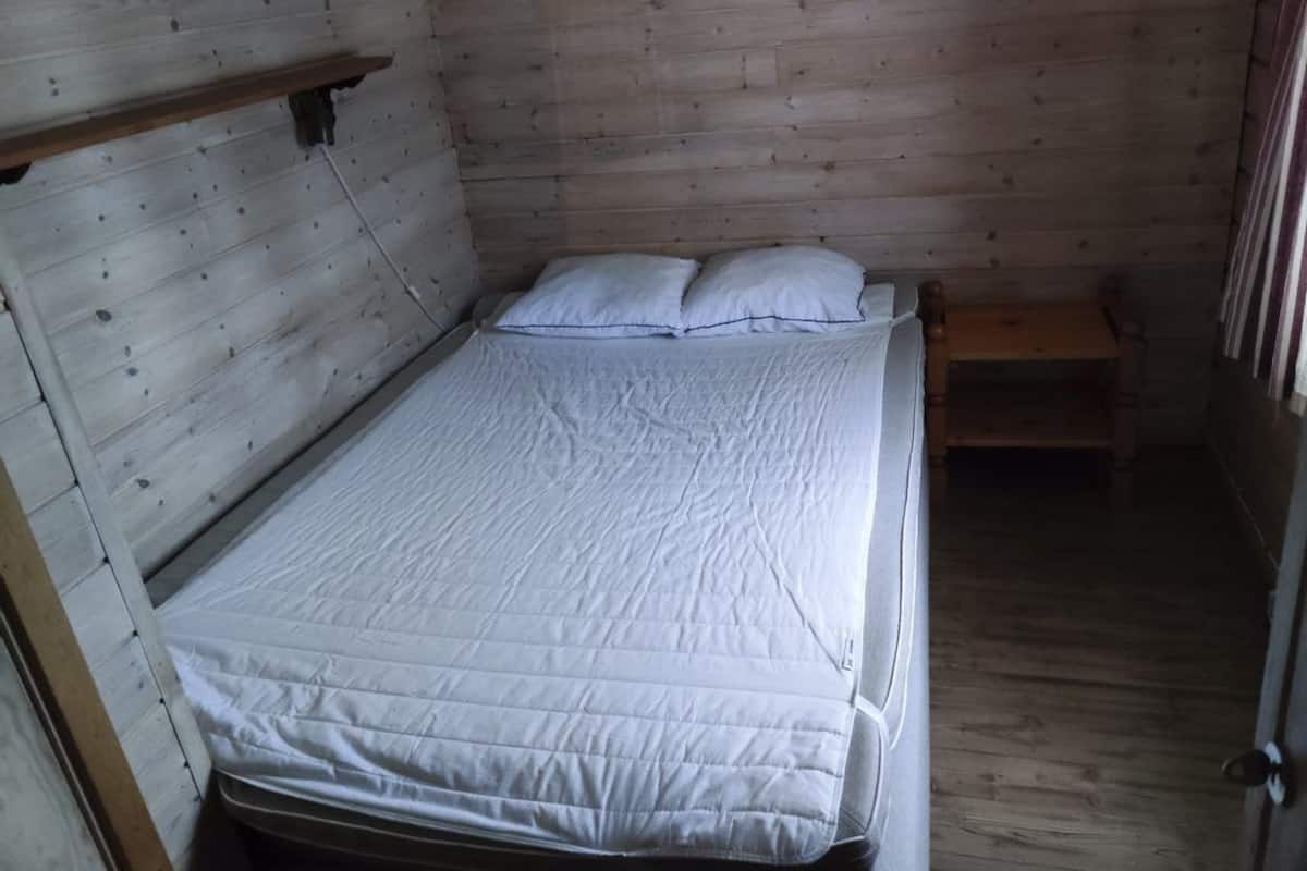 A small, single-bed room with a wooden headboard, a bedside table, and a window with curtains.