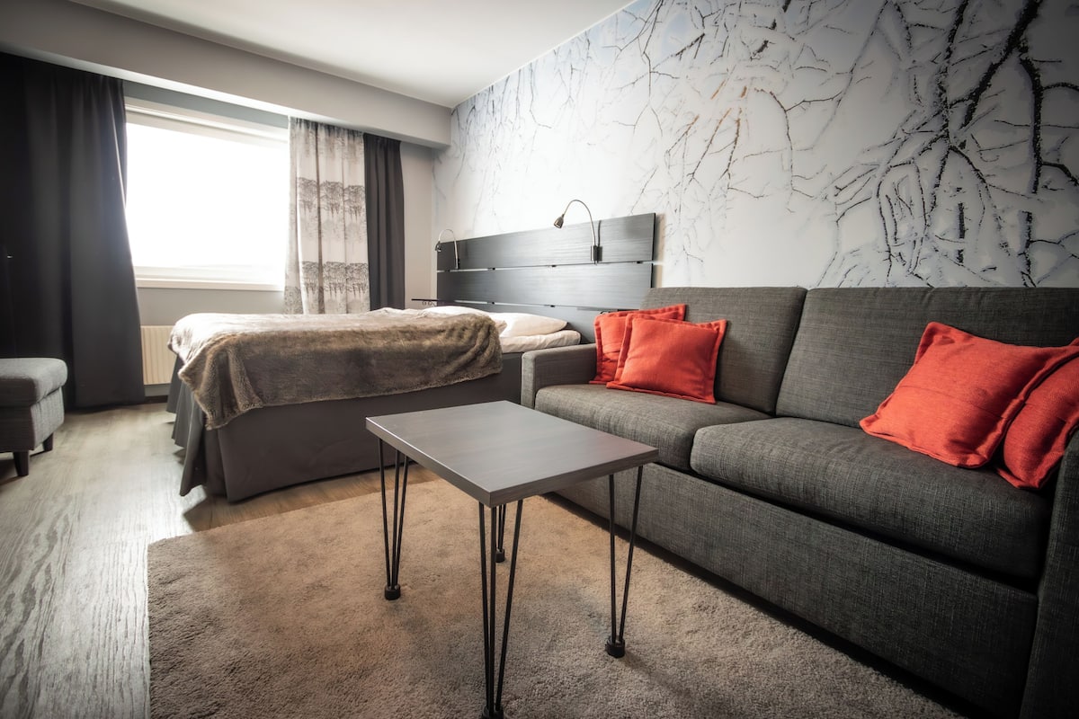 A modern hotel room with a bed, sofa, and a small table.