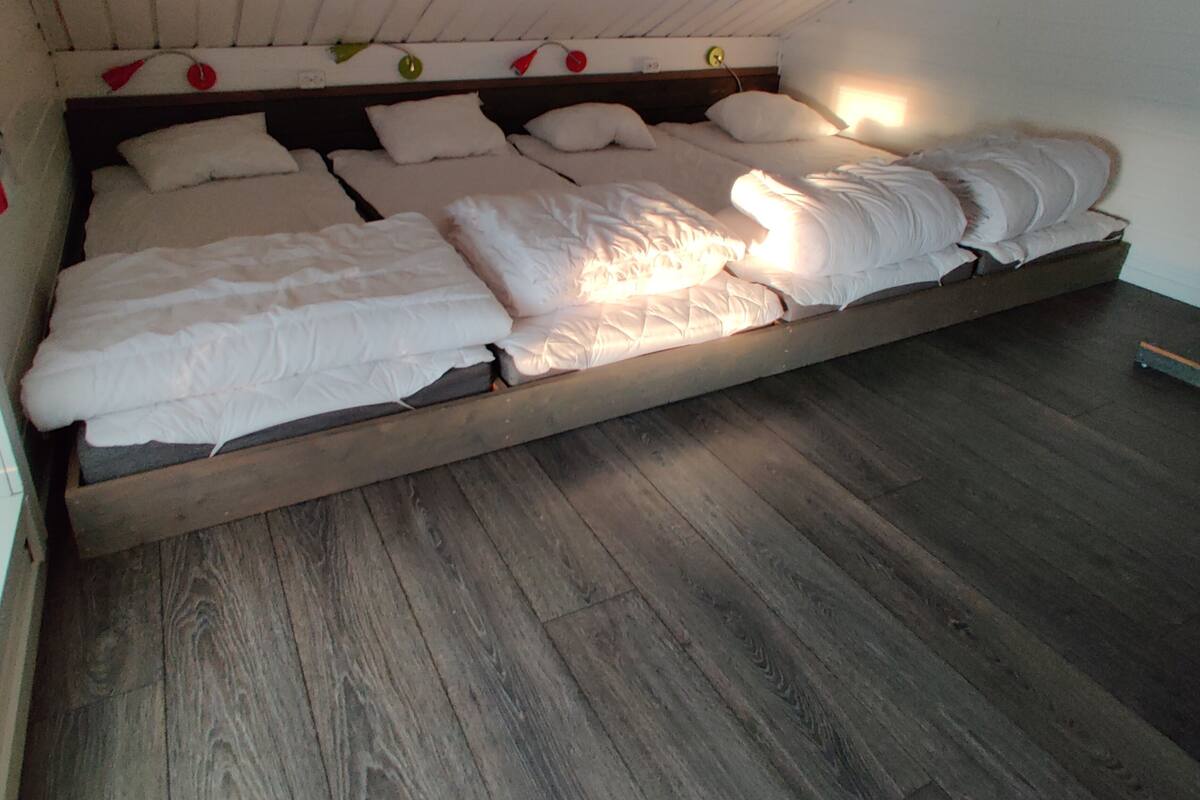 A bunk bed with white bedding, wooden beams, and a wooden floor.