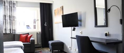A modern hotel room with a bed, a desk, a chair, a TV, and a window with curtains.