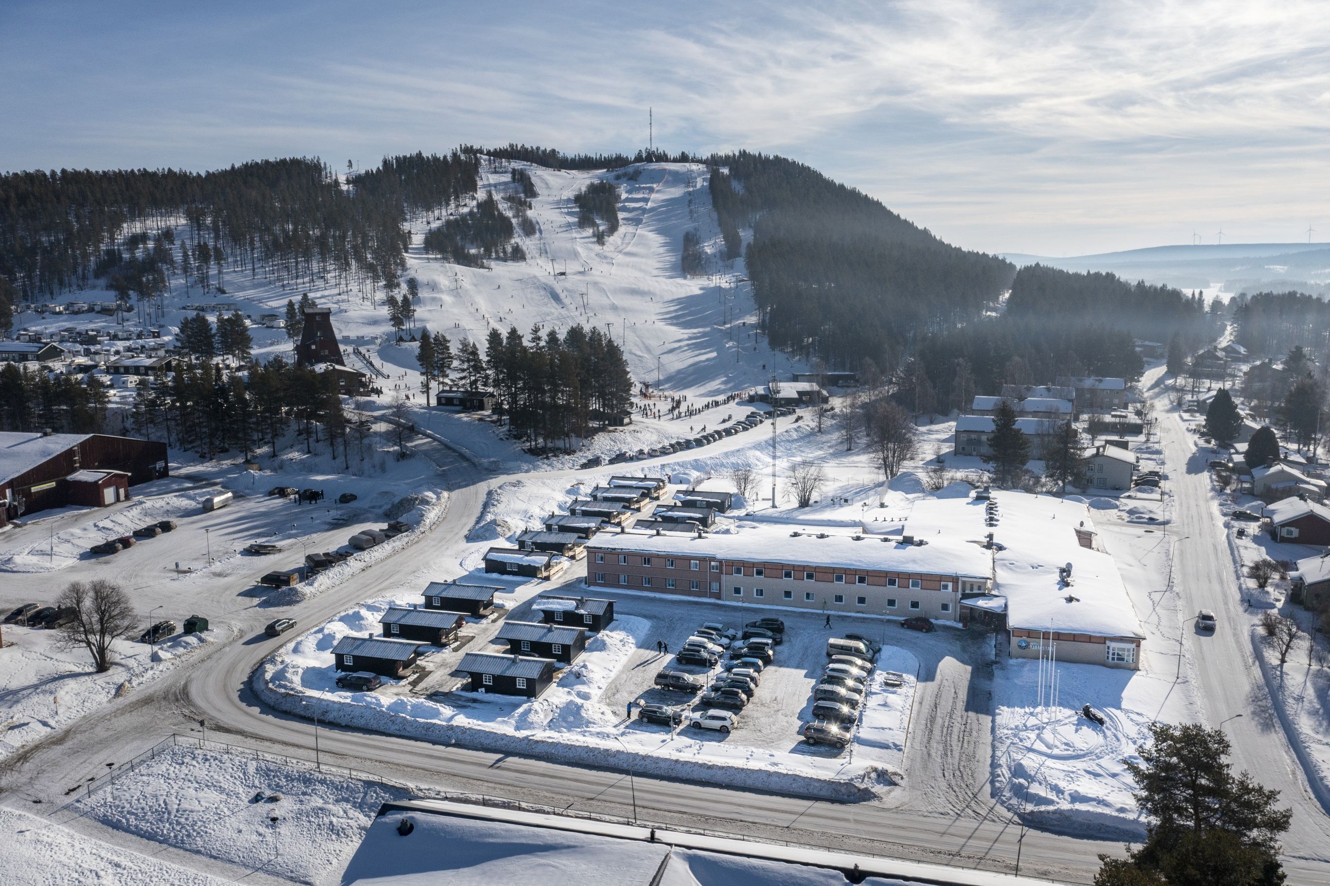 A snow-covered landscape with a ski resort, buildings, and a parking area.