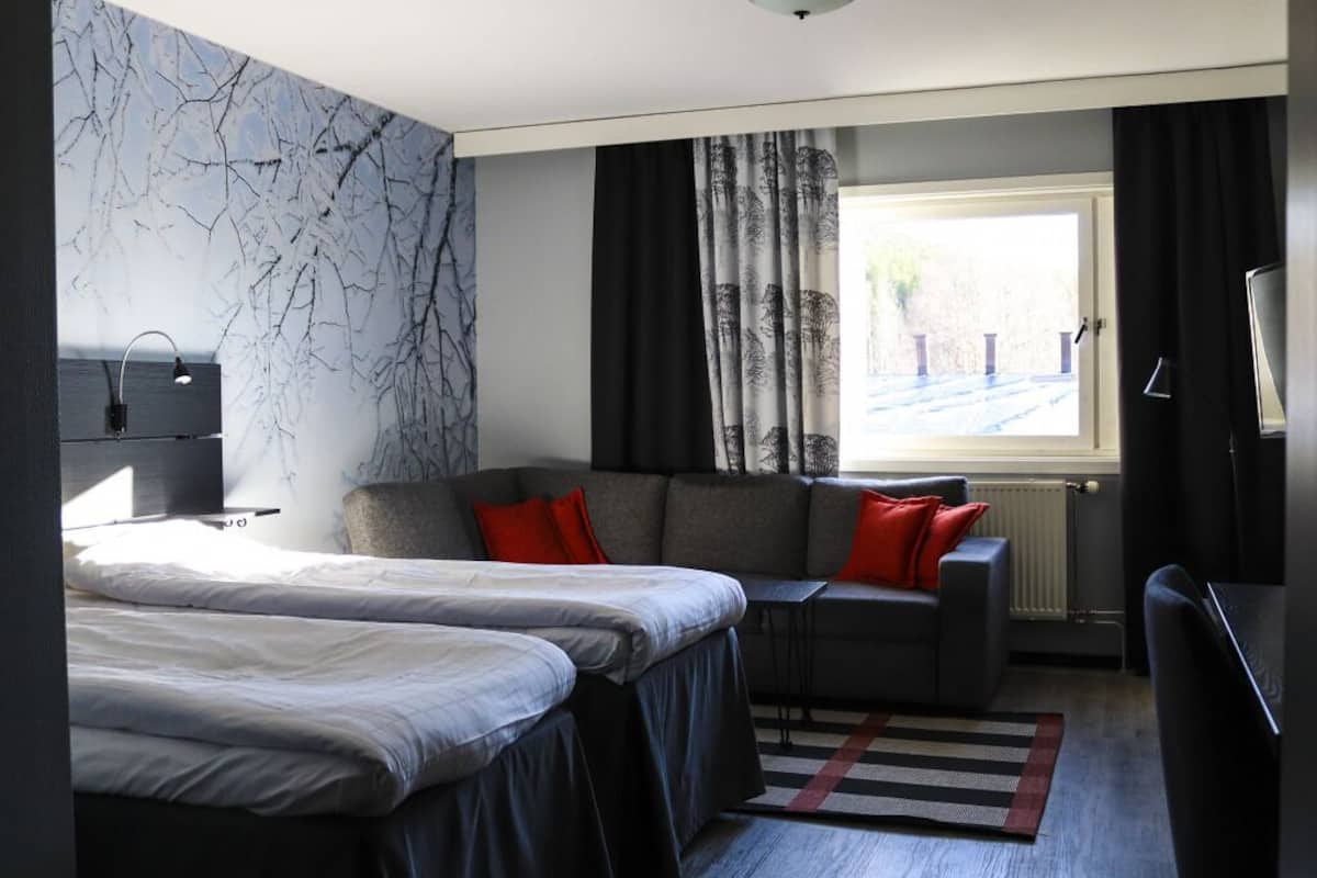 A hotel room with a bed, a sofa, a desk, a TV, and a window with curtains.