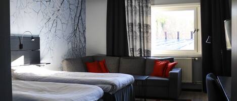 A hotel room with a bed, a sofa, a desk, a TV, and a window with curtains.