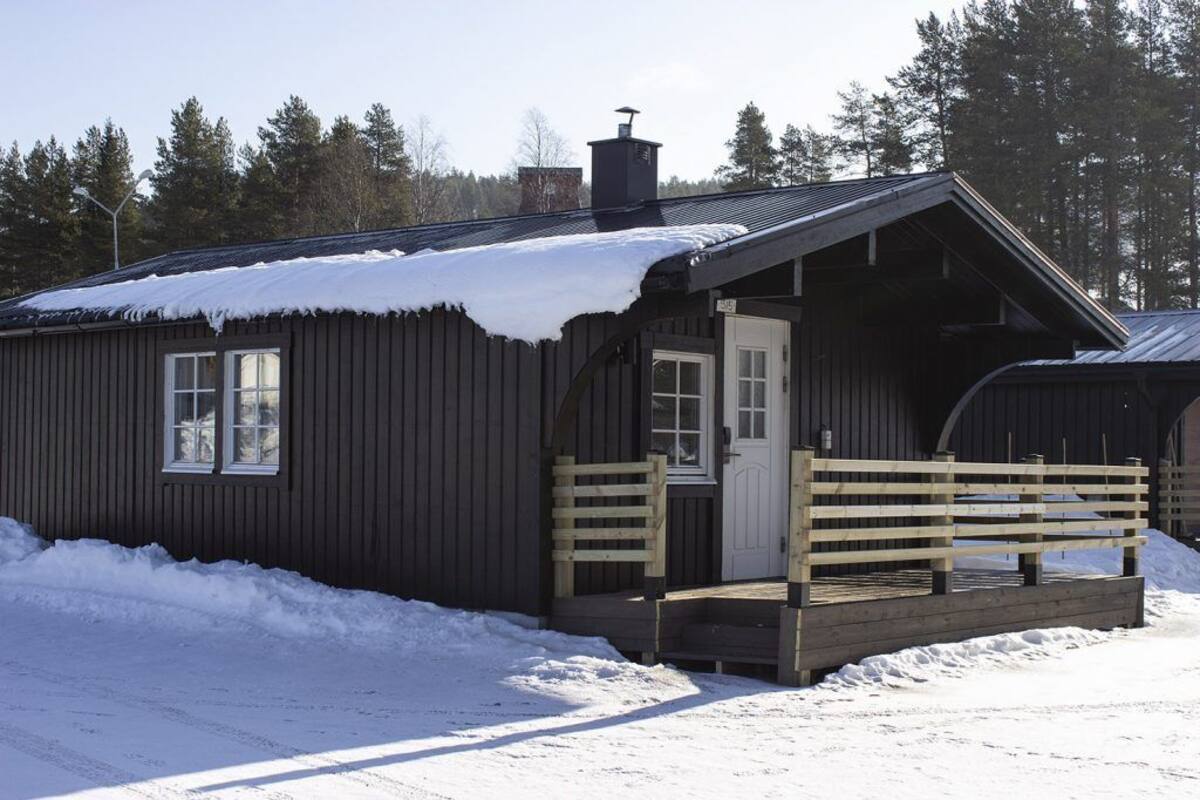 A wooden cabin with a porch, a door, and a chimney.