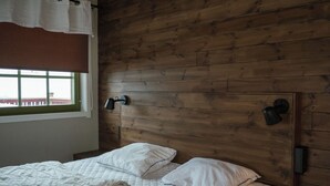 Makuuhuoneessa on puinen sängynpääty, ikkunasta avautuu kaunis näkymä ja sängyssä on valkoiset vuodevaatteet.